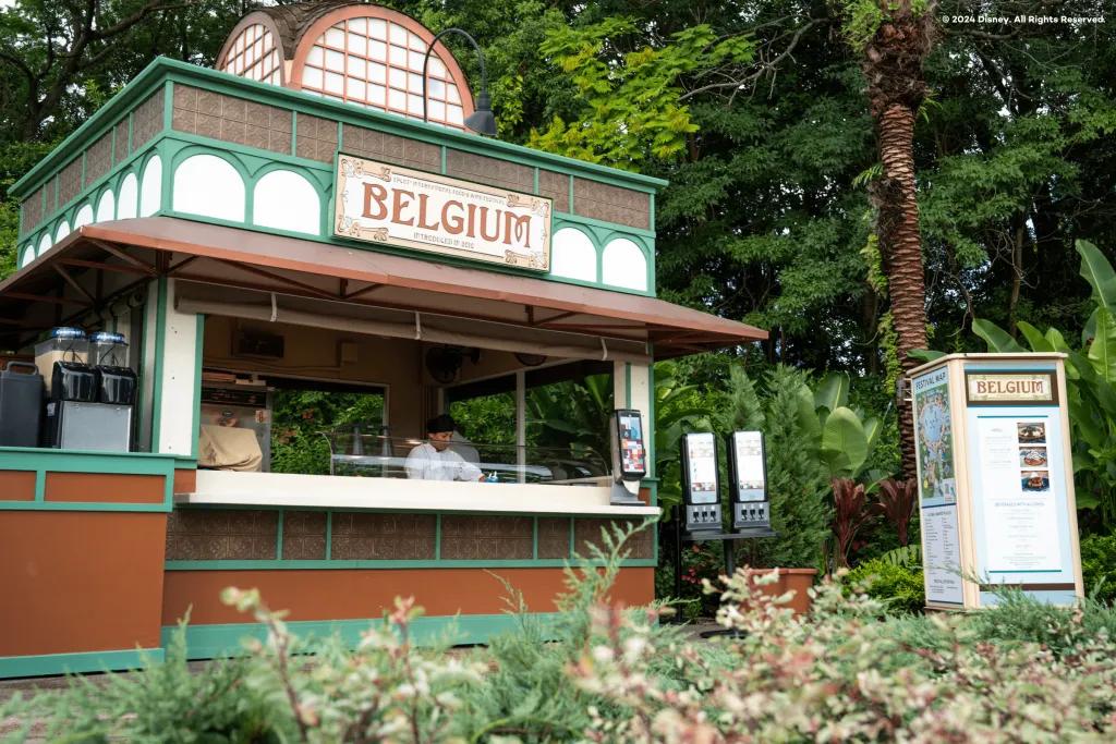 Belgium Food Stand EPCOT A food stand designed in white and green colours. There is a sign on top saying Belgium in orange. Inside there is a man in a white uniform.