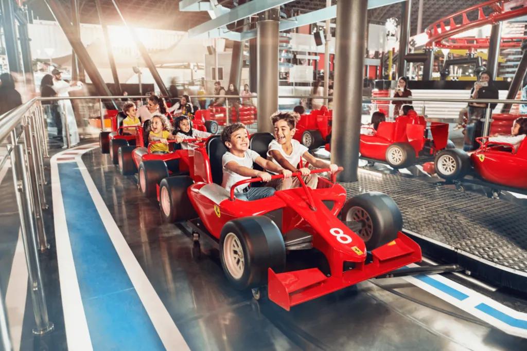 Ferrari World Little ride with small ferrari's lined up on a track. There are small kids sat on this ride holding onto pretend steering wheels.