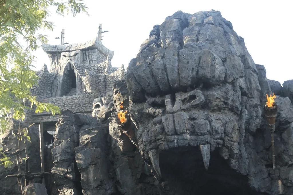 Skull Island: Reign of Kong Giant grey rock shaped like gorilla face roaring. The mouth is a cave opening and either side of the entrance there are fire torches.
