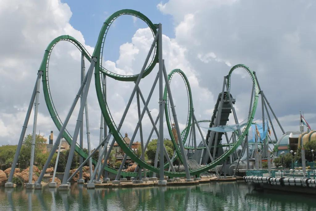 The Incredible Hulk Coaster Green rollercoaster with large pretzel loop and a green tunnel which launches the coaster up in the air. There is a large lake beside this roller coaster.