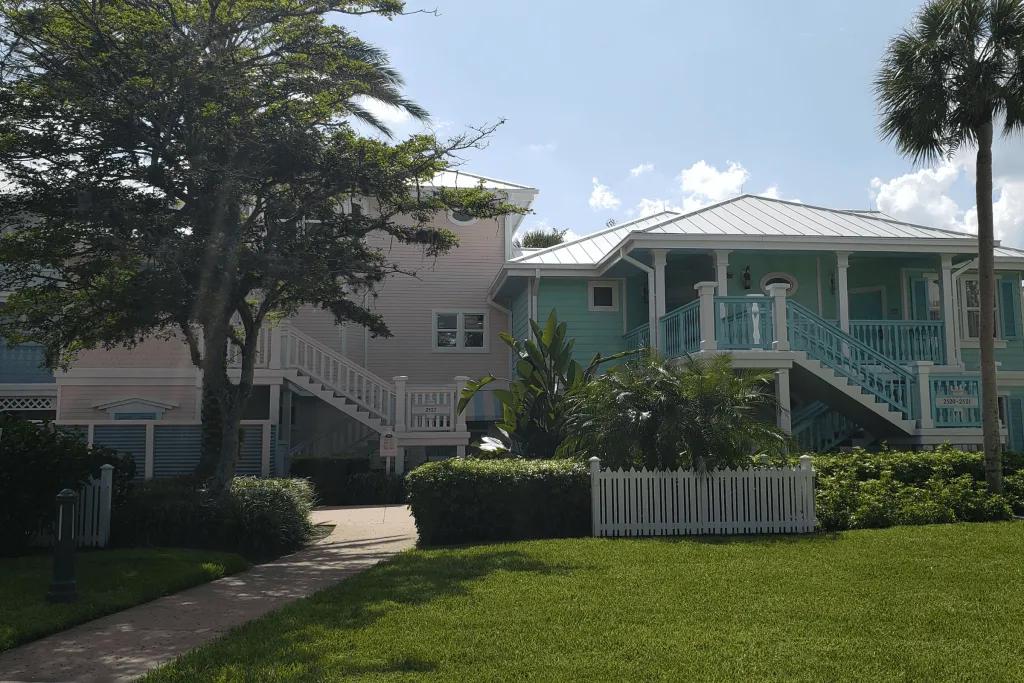 Disney's Old Key West Resort Two large coloured villas, one pastel pink and the other baby blue. The grass in front is pristine and they are decorated with white panels.