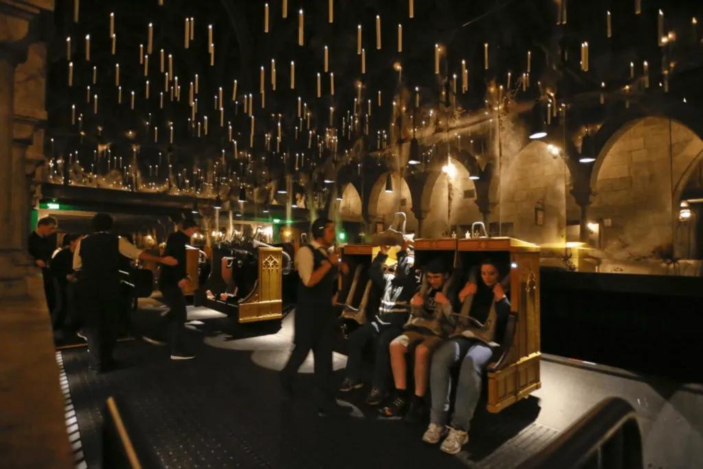 Harry Potter and the Forbidden Journey A dark room with floating candles over head. There are attendants holding torches as they strap guests into the ride vehicle safely. There are four chairs in a row.