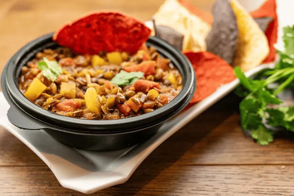 Linsen Chilli Eine Schüssel Linsen-Chili mit Tortilla-Chips als Beilage