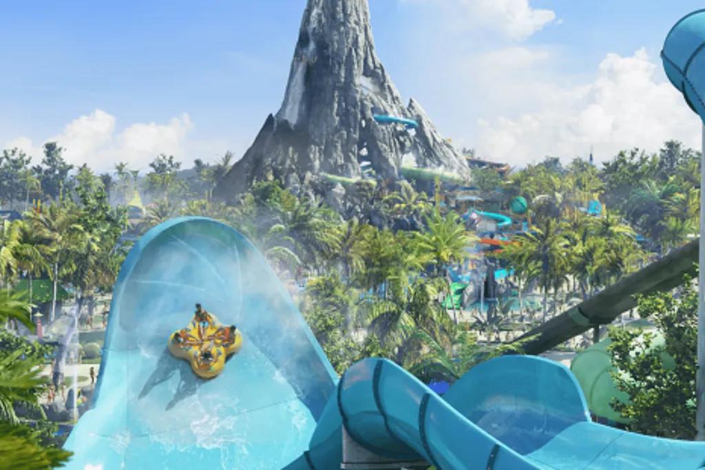 Honu, Volcano Bay Four people facing each other on a large yellow rubber ring flying up a light blue water slide wall which is huge. In the background, there is a volcano statue with slides coming off of it and water.
