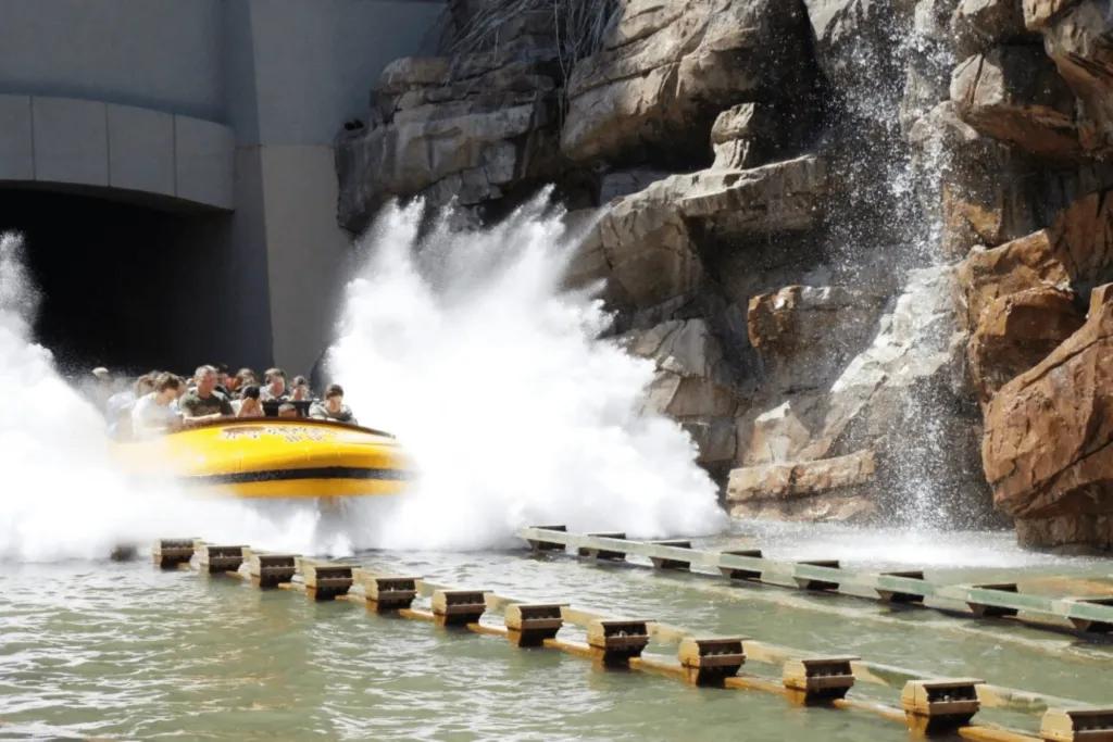 Jurassic Park River Adventure Big yellow boat splashing into a large body of water after plummeting down tall drop.