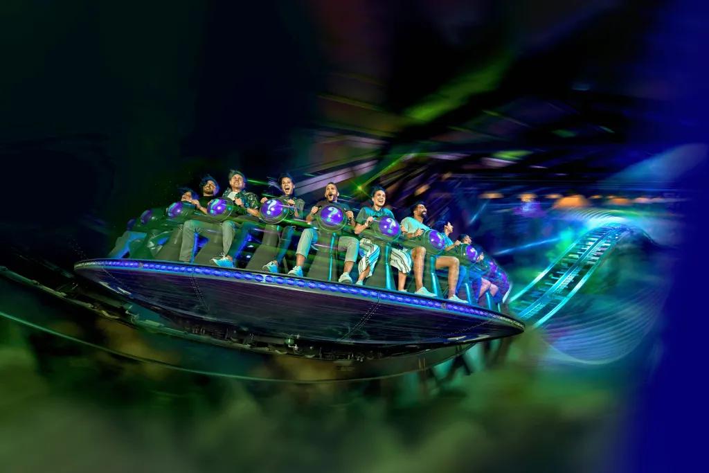 The Riddler Revolution People sat on circular vehicle facing outwards and spinning, strapped onto vehicle with back restraint. The colour scheme is blue and green.