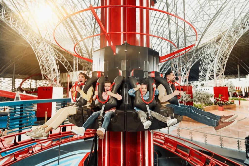 Turbo Tower A circular drop tower inside of a large industrial white building. There are small kids and adults on the drop tower smiling and screaming.