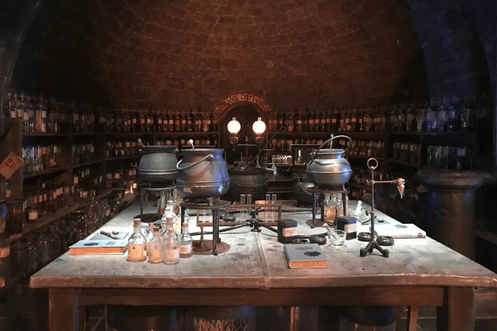 Warner Bros. Studio Tour London – The Making of Harry Potter A dark lit room with a dimly lit main table with multiple black cauldrons and substances. In the background there are dark shelves holding test tubes with different potions and substances.