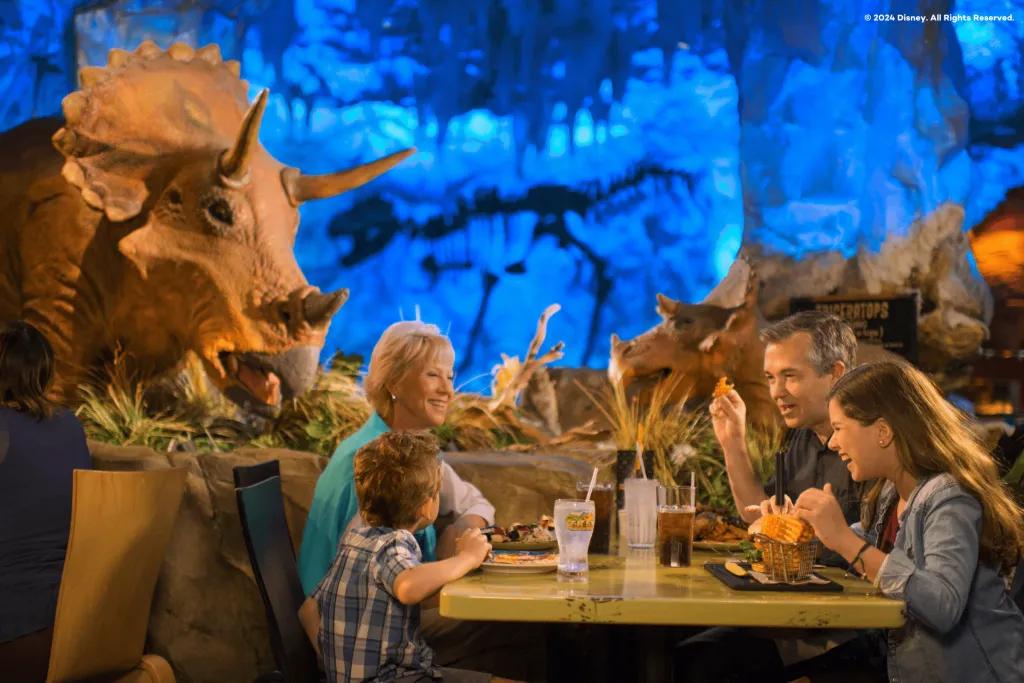 T-REX in Disney Springs Grandparents and two children laughing eating burgers and fries with dinosaur statues and skeletons behind them on display.
