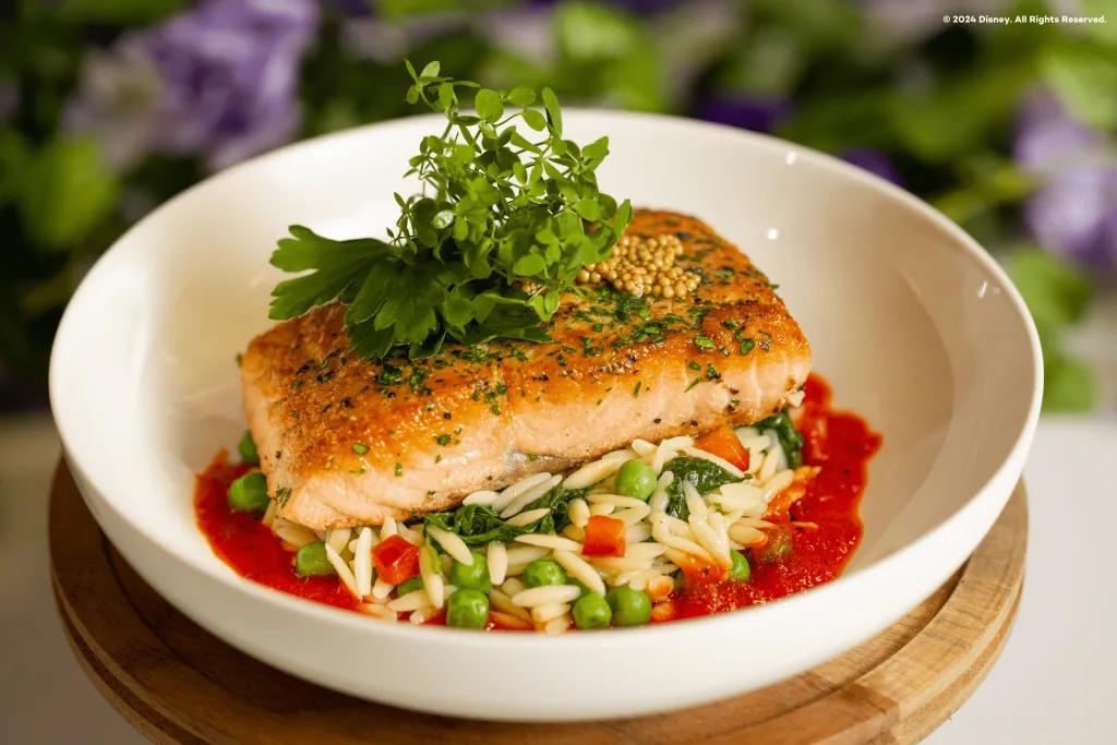 Dish in the Dining Plans Beautiful dish of salmon presented with leaves on top and ride and peas below and a red tomato sauce below on a bowl. Behind there is a bush.