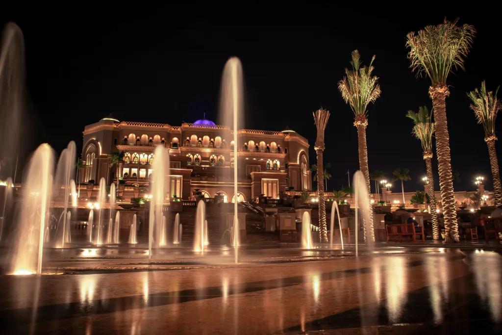 Emirates Palace Mandarin Oriental A grand hotel which looks big enough to be a palace with fountains in front, some about 10 foot tall and one in the centre approximately 20 feet tall. The building is lit in the night time a golden colour, as are the fountains. There is a small dome on the roof which is coloured blue.