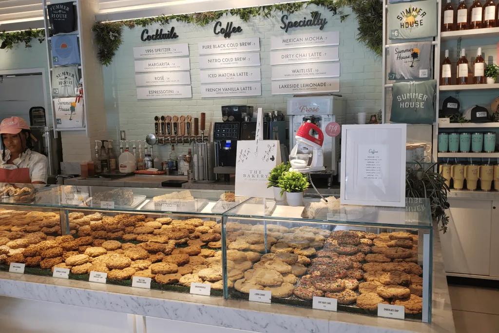 Summer House on the Lake A bakery counter with an array of different huge cookies, a mixer machine on top and behind the counter there's loads of menus showing the different food and drink options.
