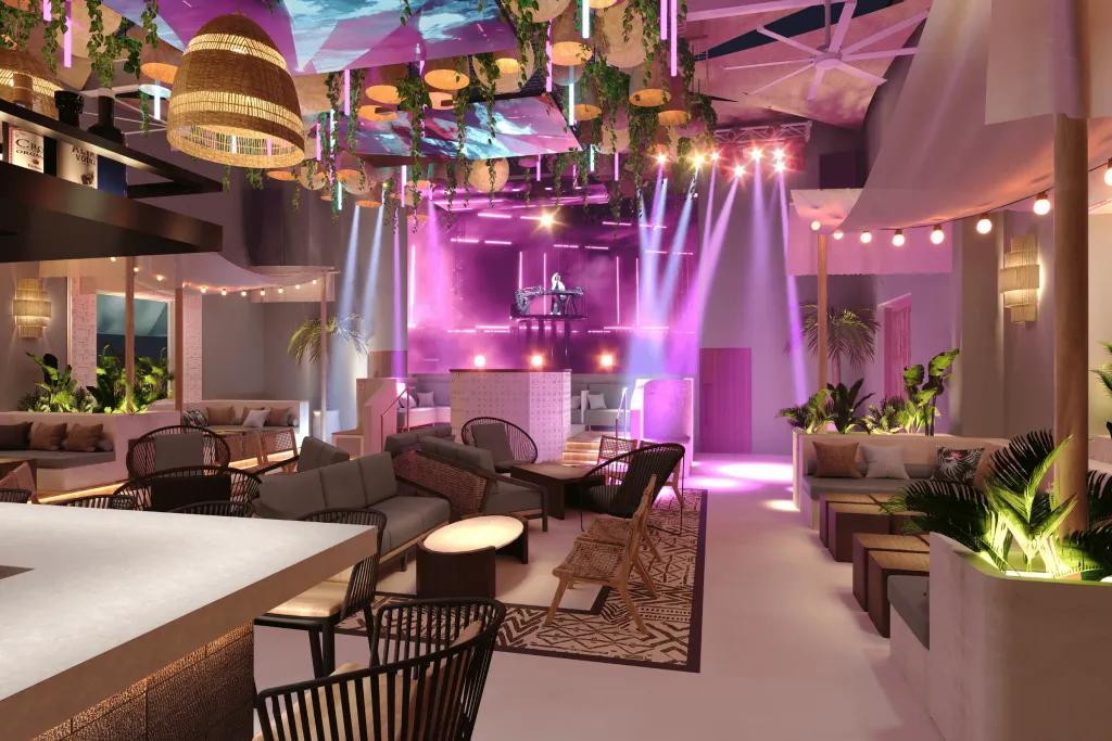 The Palm Tree Club There is a modern bar with black stools and a white bar top. There are large beige lights and a quirky curved ceiling. There are pink performance spotlights coming down on top of a dj deck.