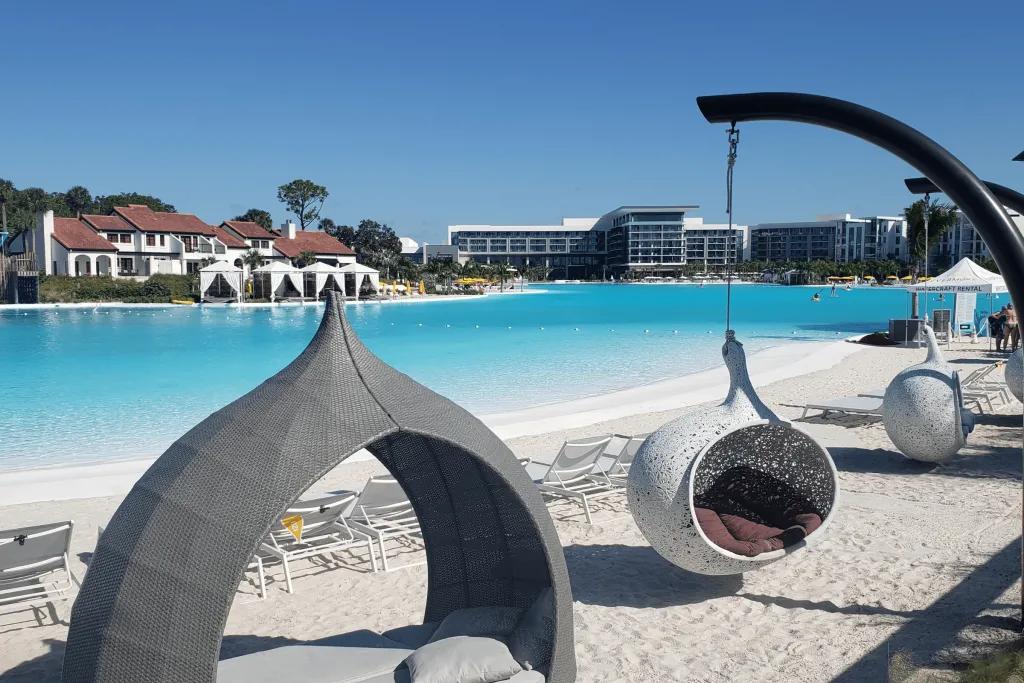 Evermore Resort Beach Tear drop shaped hammocks and sun beds made to create shade for guests. They are different shades of grey. A couple are hanging. They are on white sand with white deck chairs behind overlooking the beautiful crystal clear swimming pool.