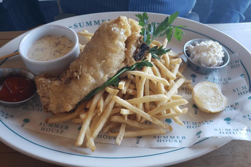 Fish and Chips at the Summer House on the Lake There's a plate with the name of the restaurant written on it. There is a delicious serving of fish and chips with pots of sauces next to it.