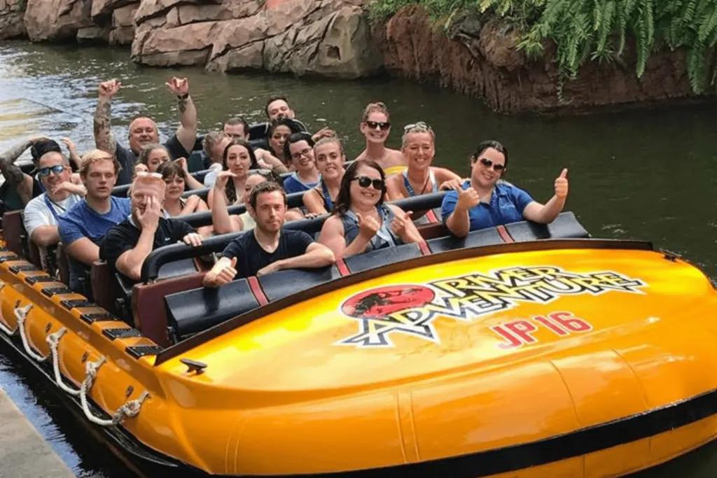 Jurassic Park River Adventure A large yellow river raft which says Jurassic Park River Adventure on the front. Riders look happy with their arms up in the photo.
