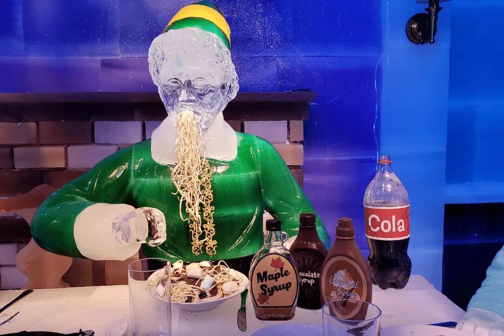 ICE! at Gaylord Palms Resort Recreation of scene from Elf movie, with an ice sculpture of Buddy the Elf scoffing down a bowl of spaghetti covered in chocolate sauce, maple syrup, marshmallows and other sweet treats. There is also a half drunk bottle of cola.