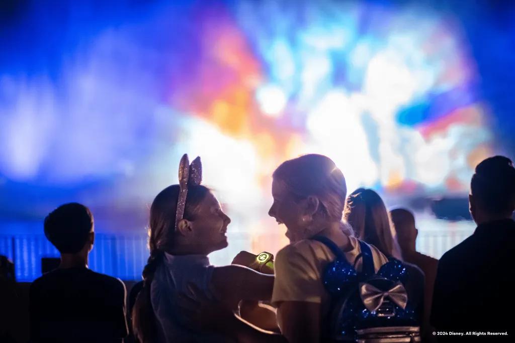 Fantasmic! Two little girls smiling and gasping looking at one another and in front of them are giant fountains with Disney movies projected onto them