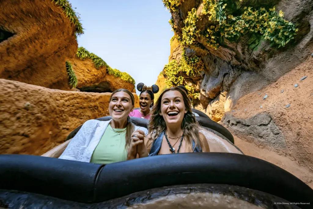 Tiana's Bayou Adventure Wasserbahn Zwei junge Frauen halten sich an den Händen und lächeln während Sie auf einer Wasserrutsche sind, kurz vor der Abfahrt steht.
