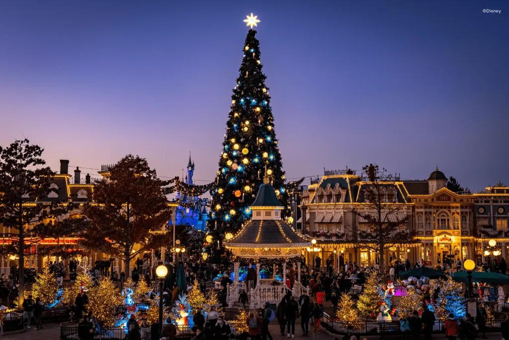 Disneyland Paris Christmas Sun setting over a theme park with a huge christmas tree in the centre of old fashioned buildings.