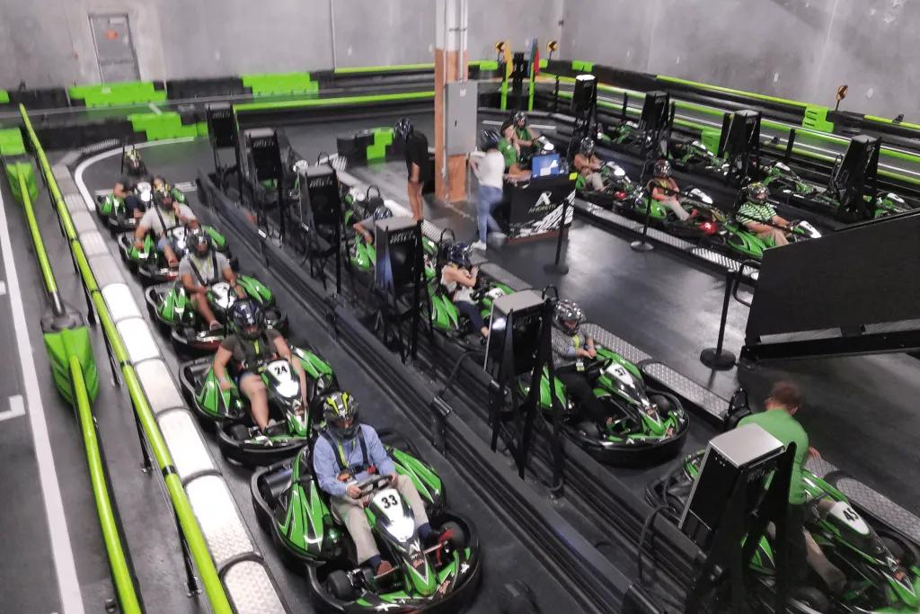 Andretti Indoor Karting & Games Black and green go karts with people sat in them waiting to start their race. There is a black track and they are all wearing helmets.
