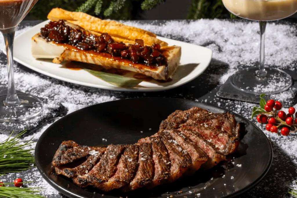 STK Christmas A black plate with steak cooked medium well, some bread with a sauce on it and a glass of wine on the side.
