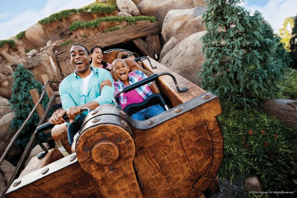 Seven Dwarfs Mine Train Guests sat in a mine cart coming out of a rock cave screaming and smiling.