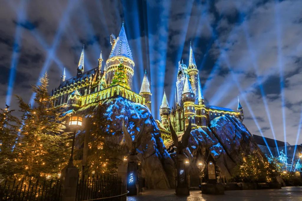 Hogwarts Christmas Hogwarts castle lit up in projections of golden christmas trees with loads of spotlights shooting up into the nightsky.