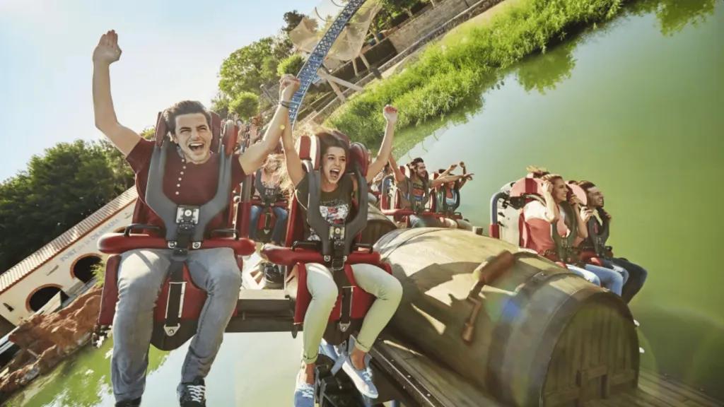 Furius Baco im PortAventura Park Ein Mann und eine Frau sitzen mit gehobenen Armen und breitem Lächeln auf einer Achterbahn