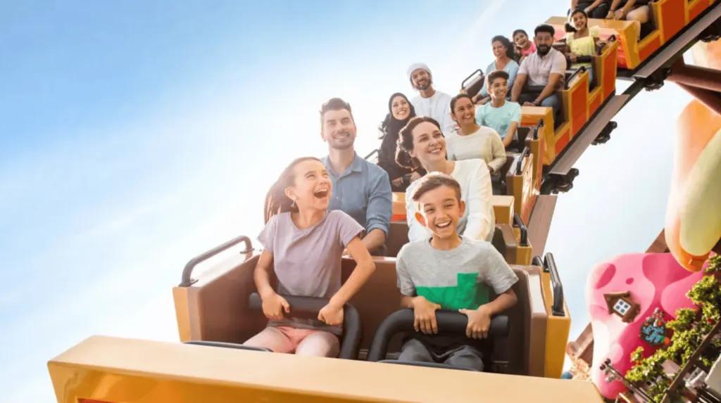 MOTIONGATE Dubai Lachende Personen sitzen in verschiedenen Fahrwagen auf einer bunten Achterbahn