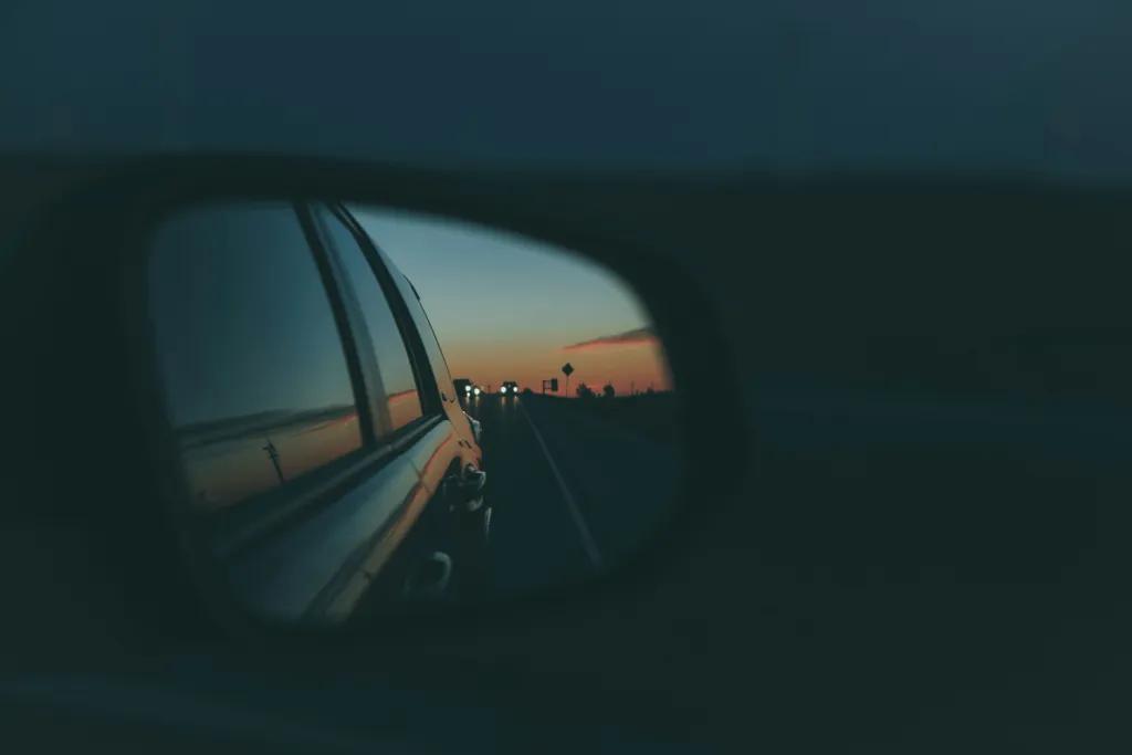 Road Trip Dark night with car mirrors and in the mirror you can see the sun setting in the background and palm trees.