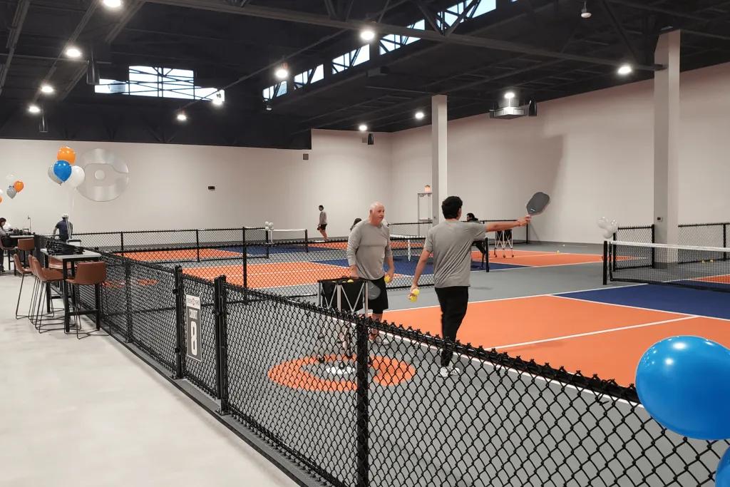 Pickleball Courts People stood with rackets drinking water in the middle of courts which are smaller than regular tennis courts.