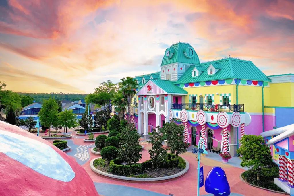 Give Kids The World Resort A large centre building coloured bright pink, yellow and turquoise shaped like a town hall. There are roads which are wheelchair accessible and a large mushroom with a carousel under it.