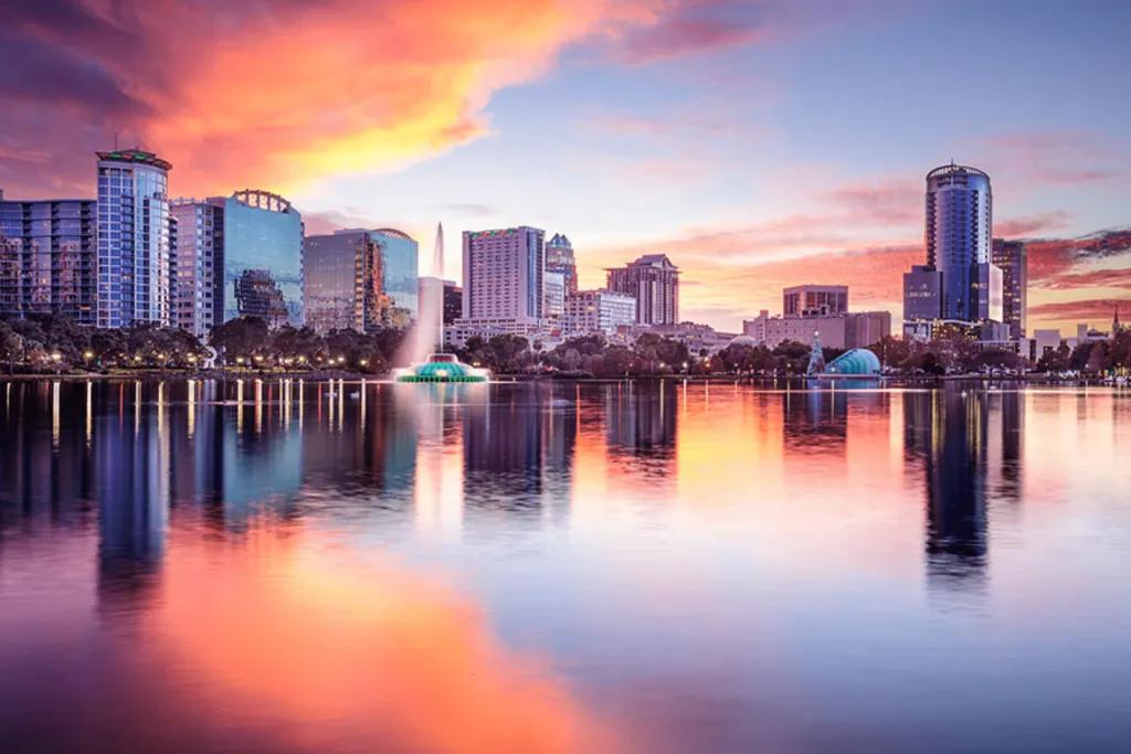 Lake Eola Park Huge lake at sunset with the orange sun reflections lighting up the sky above large glass buildings.