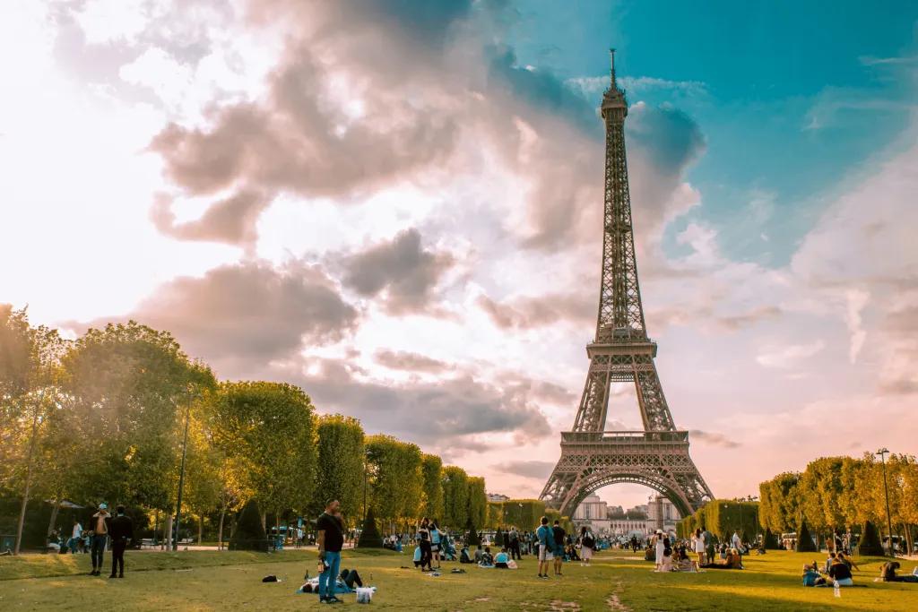 The Eiffel Tower in Paris A large steel structure shaped like a triangle with viewing platforms at the end of a long, straight park lined with trees.