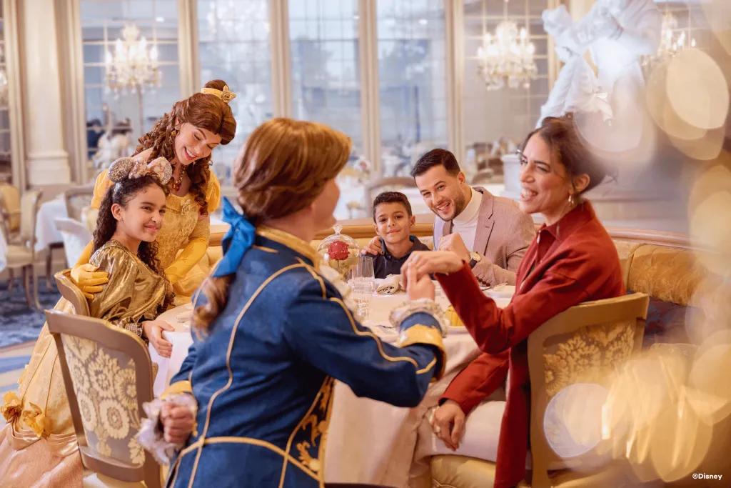 La Table de Lumiere A family sat around a table in a restaurant being greeted by Belle and her prince