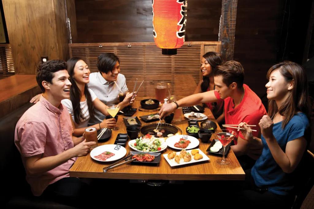 Dining in Florida Group of friends sat around a table sharing dishes and drinking alcoholic drinks in Japanese style restaurants.