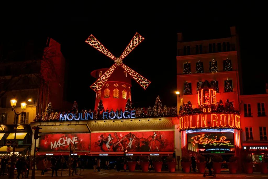 Moulin Rouge in Paris A large building lit red with a large windmill prop on top and a white sign saying Moulin Rouge