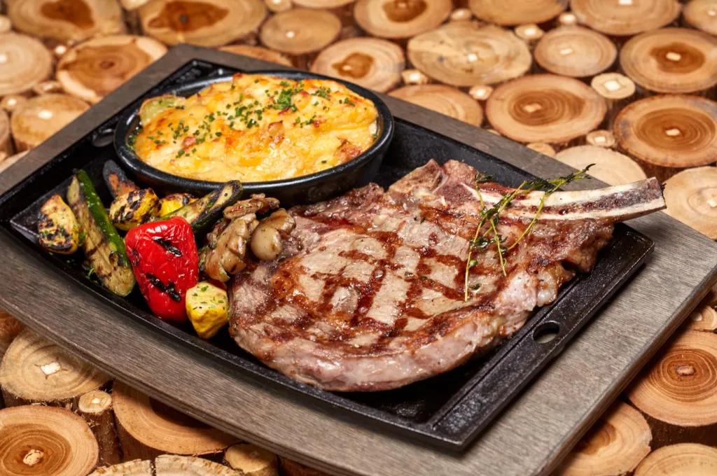 Premium Ribeye Steak A ribeye steak, baked potato gratin and roasted vegetables on a cast-iron plate