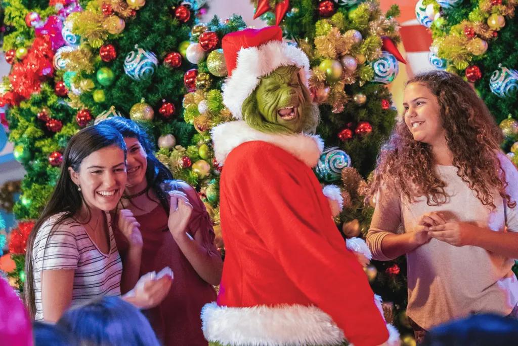 Grinchmas Three girls posing in front of a Christmas tree with the Grinch dressed as Santa