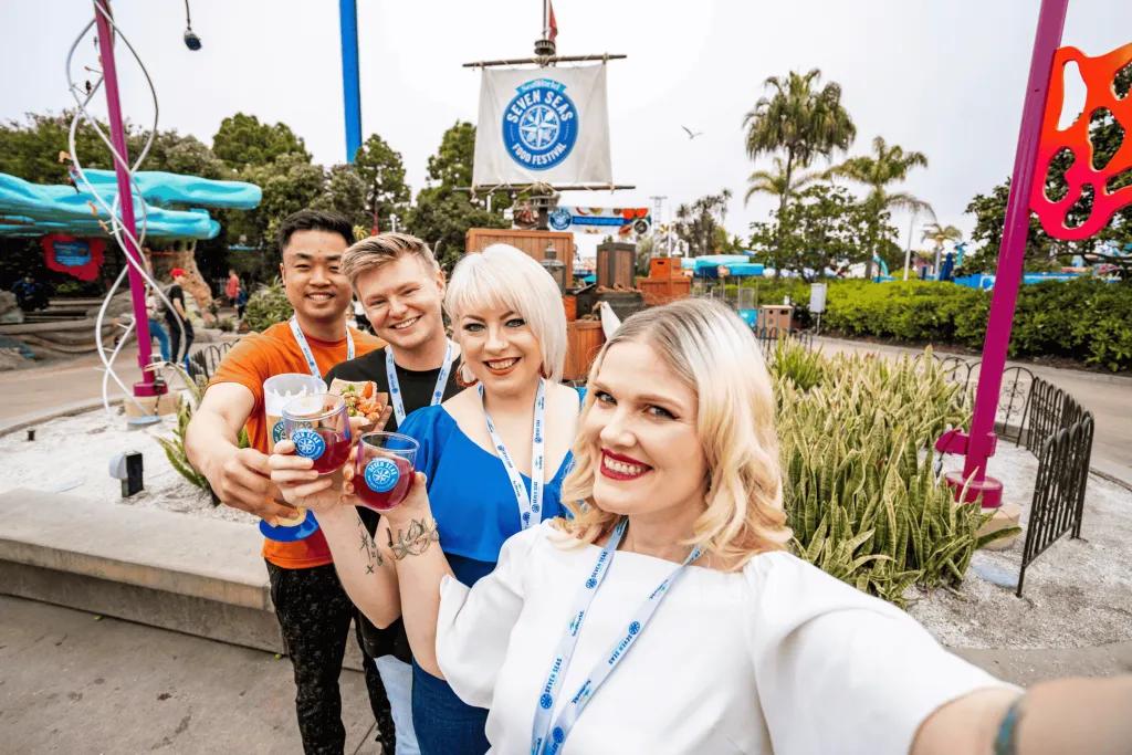 SeaWorld Seven Seas Food Festival A group of friends taking a selfie with food and drink in front of a Seven Seas Food Festival sign