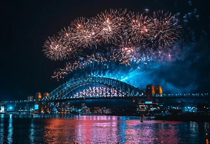Silvesterfeuerwerk in Sydney Ein Feuerwerk über der Sydney Harbour Bridge erhällt die Brücke und lässt das Wasser des Hafens rot erleuchten