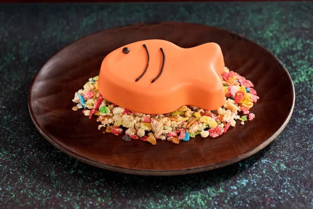 Stormfly’s Catch of the Day Dessert Ein orangefarbener Schokoladenmousse-Fisch mit braunen Details auf einem Reiskrispy-Müsliriegel.