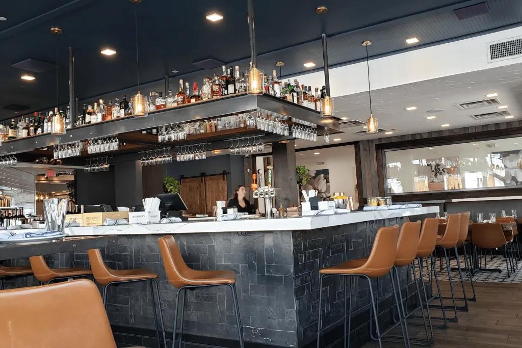Winter Garden Boca A dark grey bar with brown leather bar stools in a modern restaurant and bar.