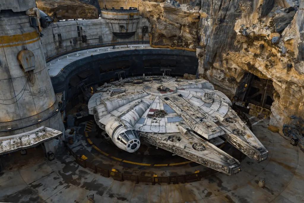 Millennium Falcon: Smuggler’s Run Millenium Falcon (a grey flat shaped space ship) parked on batuu, a mythical stone filled island.