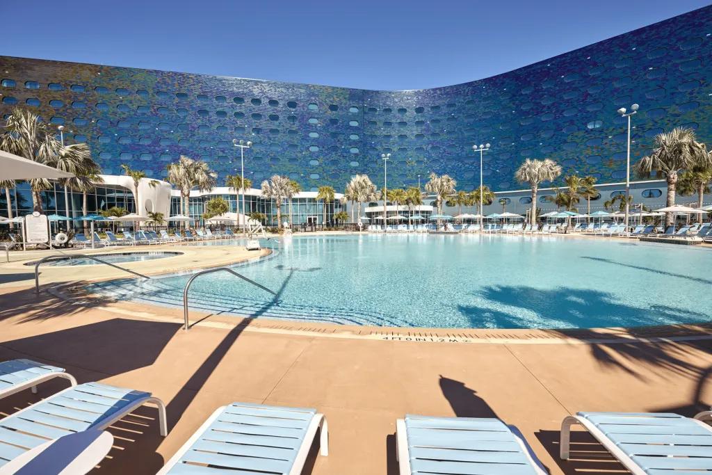 Terra Luna Resort Large hotel with blue and purple ombre tiles on the outside, with a large pool outside surrounded by white deck chairs and palm trees.