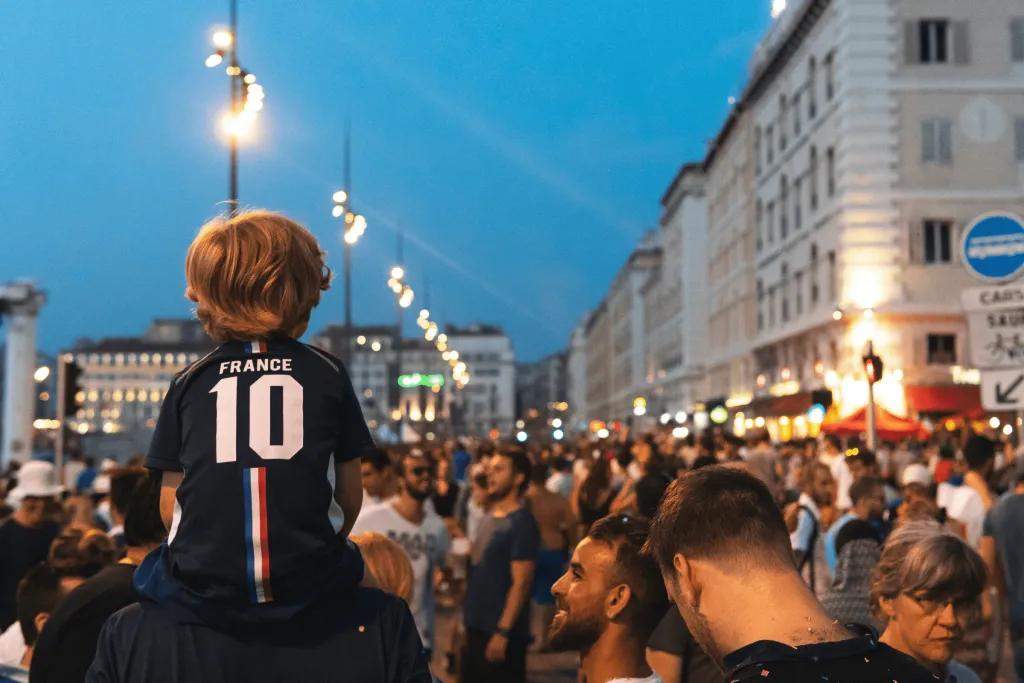 It's Coming Home! Football fans in a European city with one child on his dads shoulders wearing a football shirt with 10 on it.