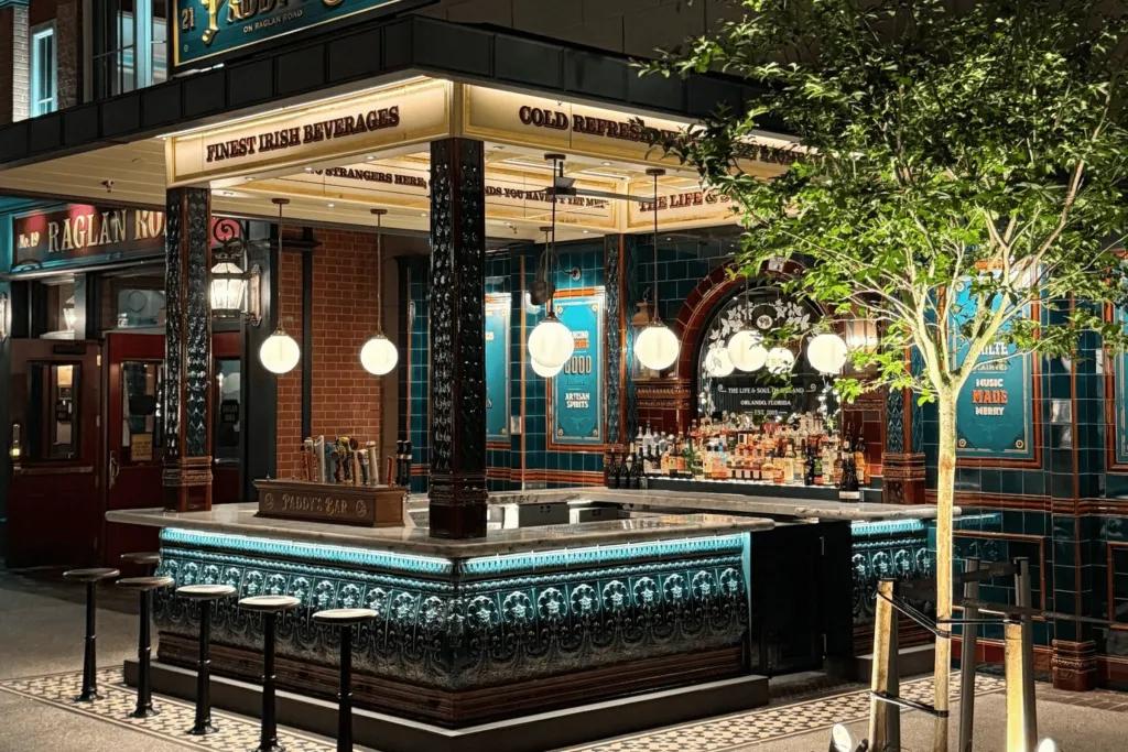 Paddy's Bar An outside bar with a modern, slick design. There are dark green/turquoise tiles on the wooden panelling and stool chairs to match. There are also low hanging circular lights below the sign.