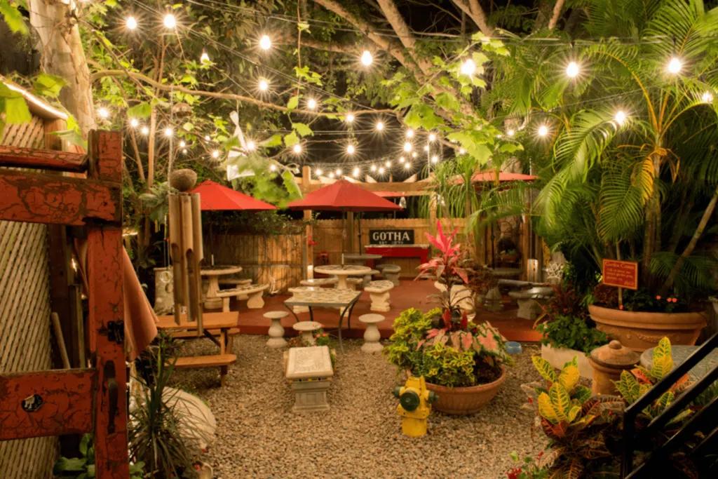 Yellow Dog Eats Vibrant patio with leaves and plants hanging overhead. It is themed like a garden with white stools and benches.