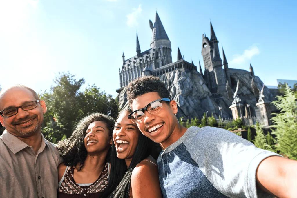 The Wizarding World of Harry Potter A family laughing and smiling in front of the grey Hogwarts castle, consisting of a mum, dad, son and daughter.